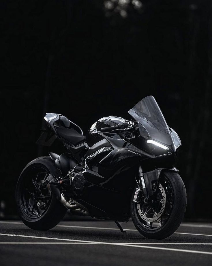 a black motorcycle parked on the street in front of some trees and dark lighting behind it