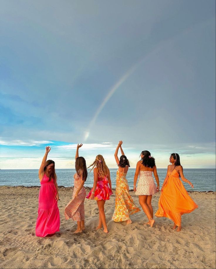 four girls are walking on the beach with their arms in the air