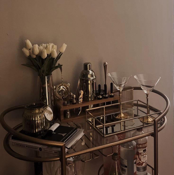 a bar cart with wine glasses and bottles on it next to a vase filled with tulips