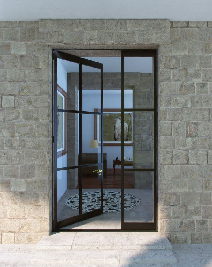 an open glass door leading to a living room with stone walls and floor tiles on the outside