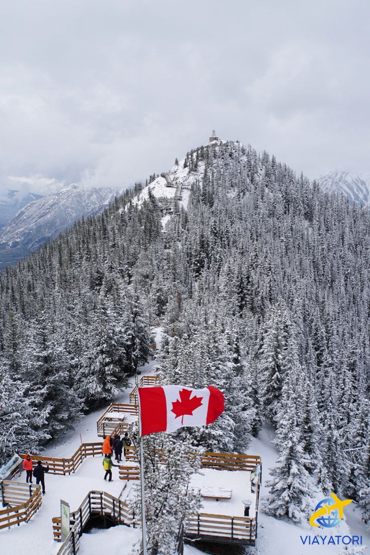 a canadian flag on top of a mountain with people standing around it and trees in the background