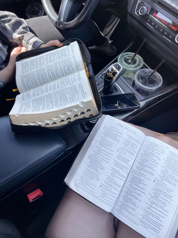 a person sitting in a car reading a book and holding an open bible with both hands