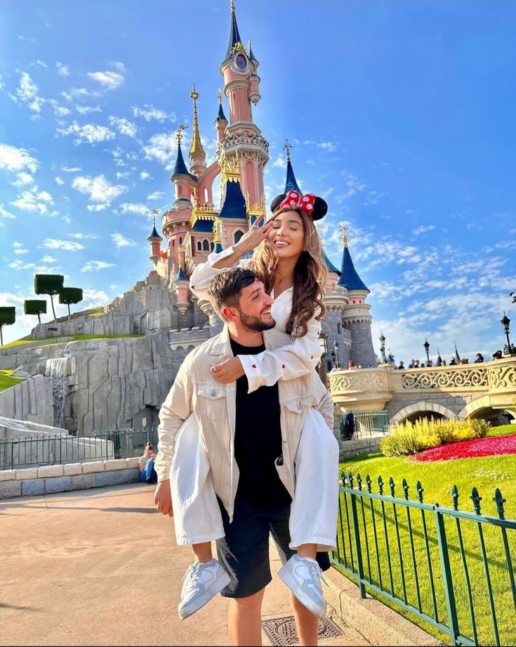 a man carrying a woman on his back in front of a castle at disneyland world