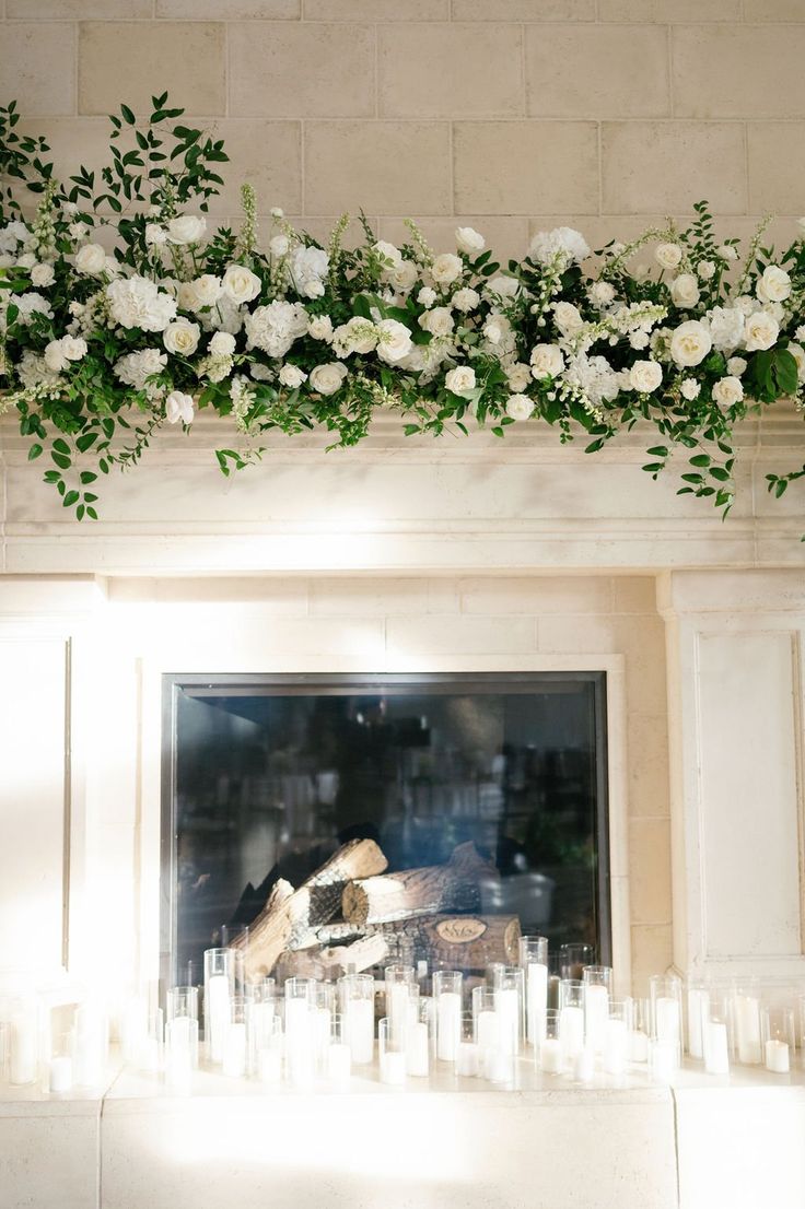 white flowers and greenery decorate the fireplace mantel