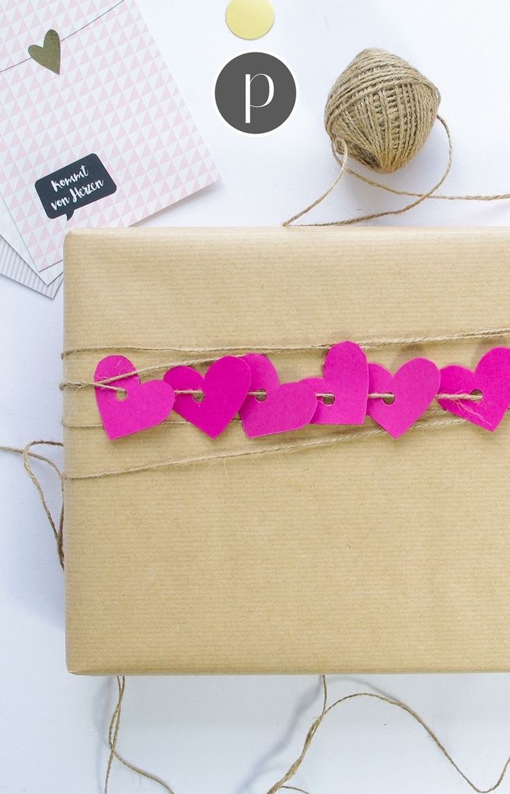 a wrapped gift with pink paper hearts on it next to twine and twine