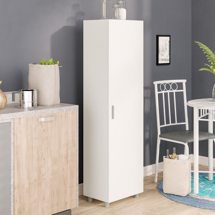 a white cabinet sitting next to a table and chairs in a room with gray walls