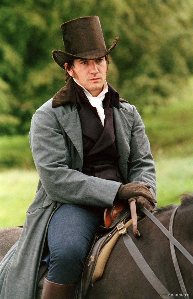 a man sitting on top of a horse wearing a black hat and coat with long sleeves