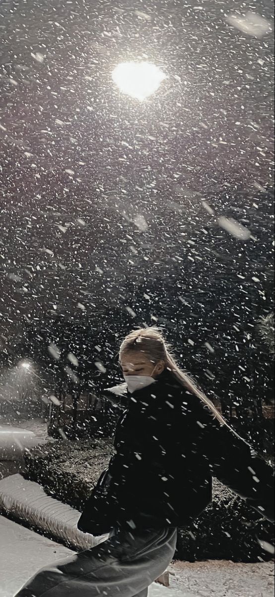 a woman sitting on top of a snow covered bench under a street light at night