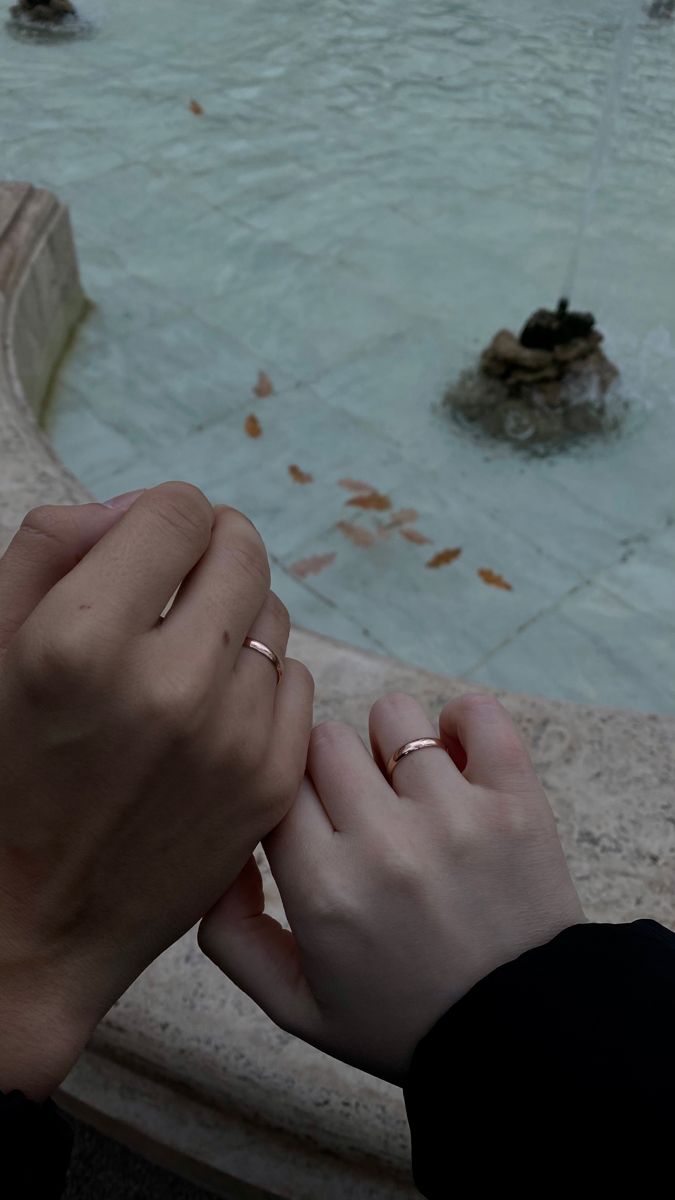 two people holding hands in front of a fountain