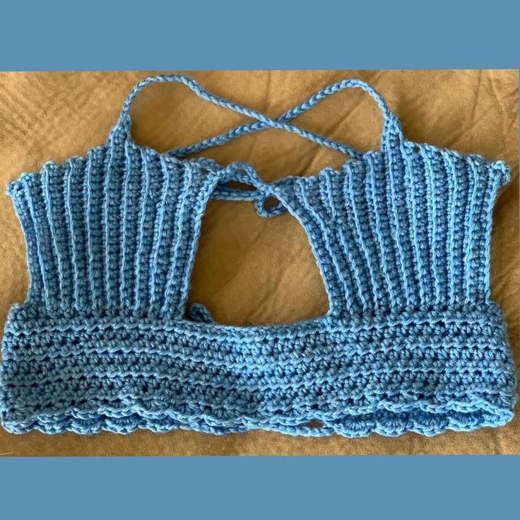 a crocheted blue top is laying on a bed and it has two ties at the back