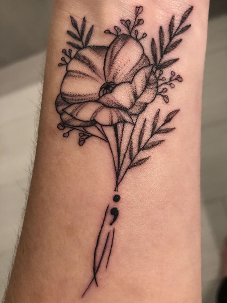 a black and white flower tattoo on the left arm, with an arrow in the center