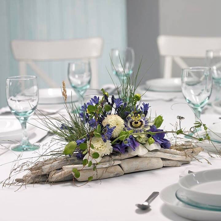 the table is set with white and blue flowers, greenery, and driftwood