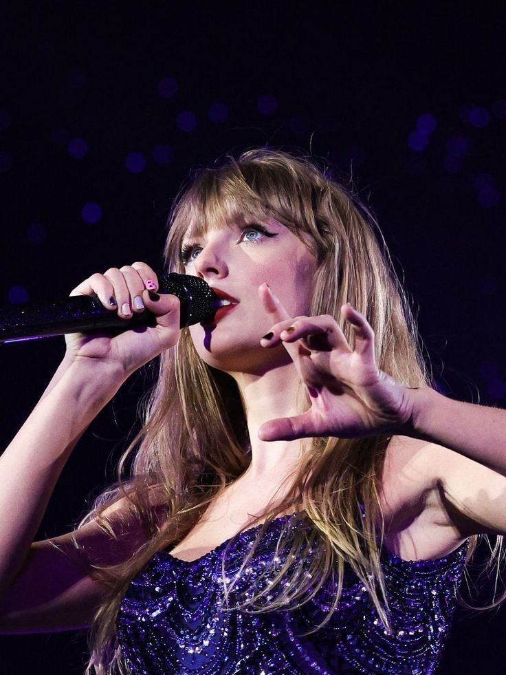 a woman in a purple dress holding a microphone up to her mouth while performing on stage