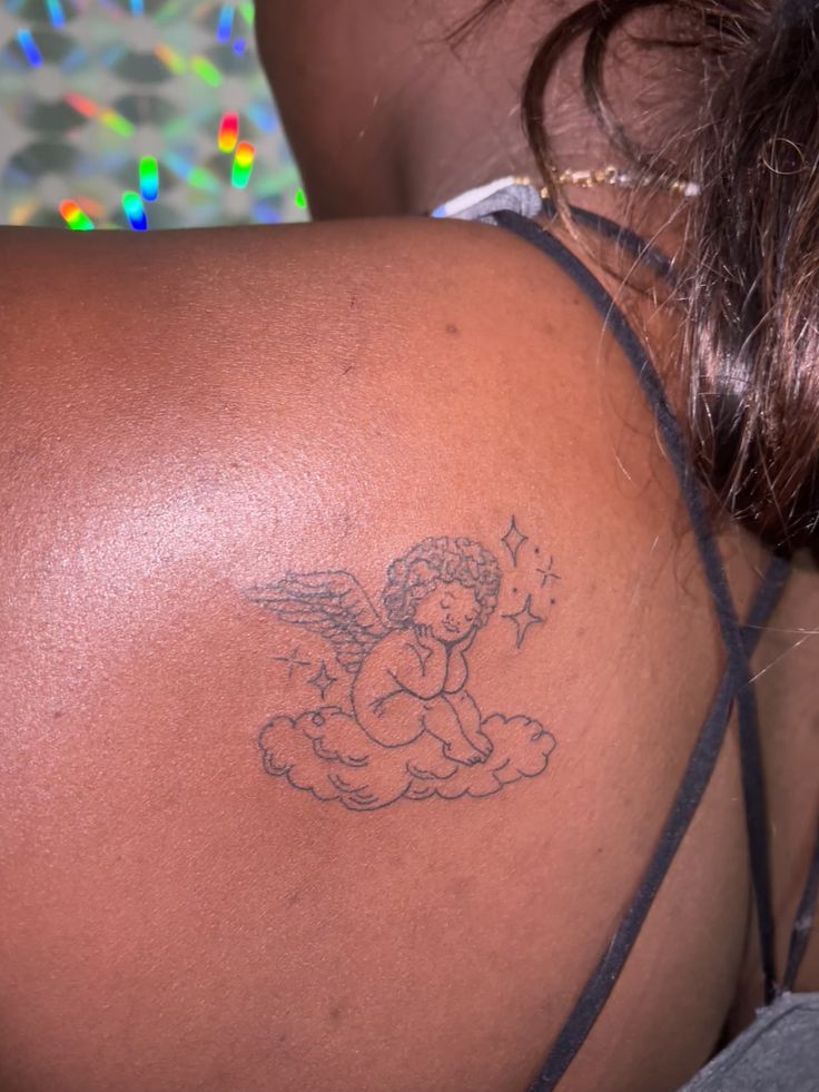 the back of a woman's shoulder with an angel tattoo on her left side