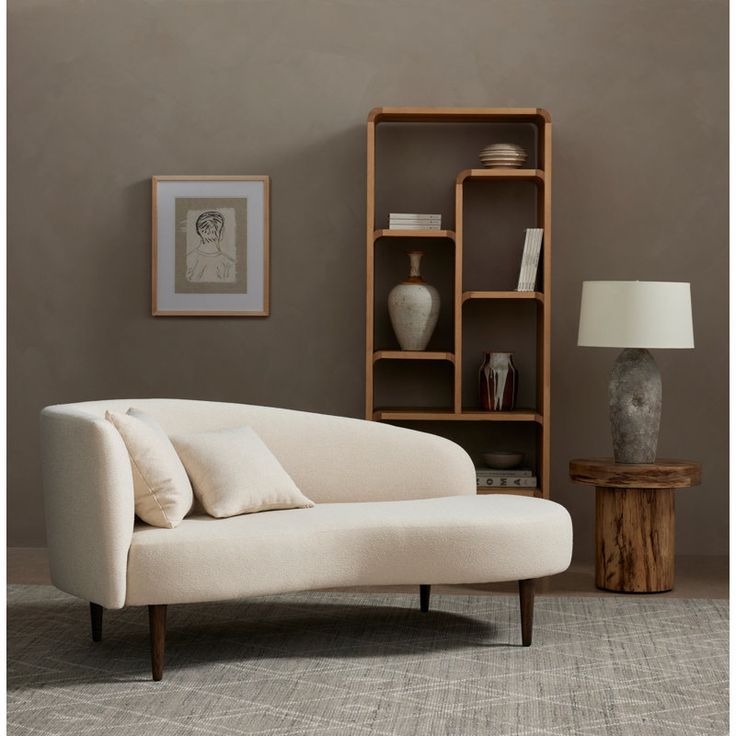 a white couch sitting in front of a wooden shelf filled with vases and books