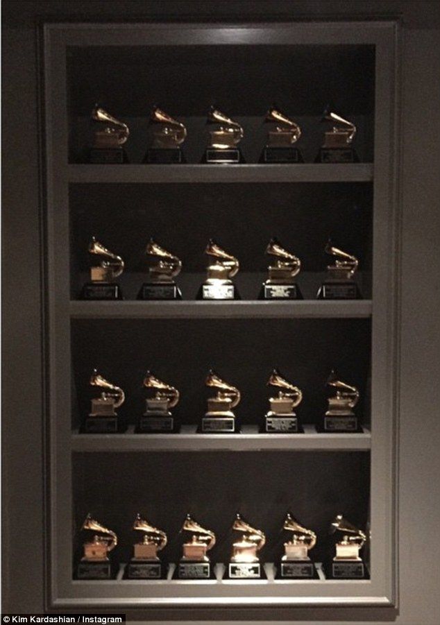 many awards are lined up on shelves in a room with black walls and white carpet