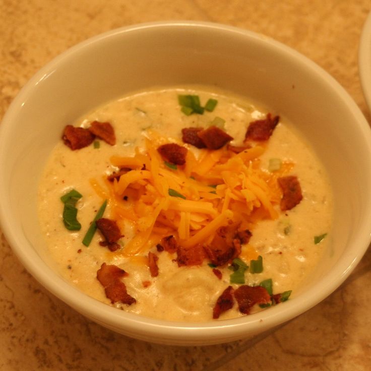 a bowl of soup with bacon and cheese in it next to a spoon on a table