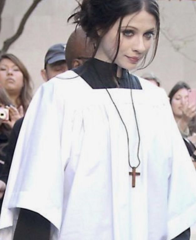 a woman in a priest's outfit walking down the street with people behind her