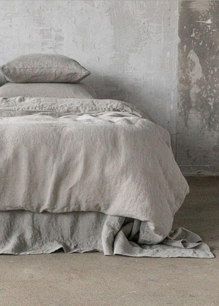 an unmade bed with two pillows on top of it in a room that has concrete walls