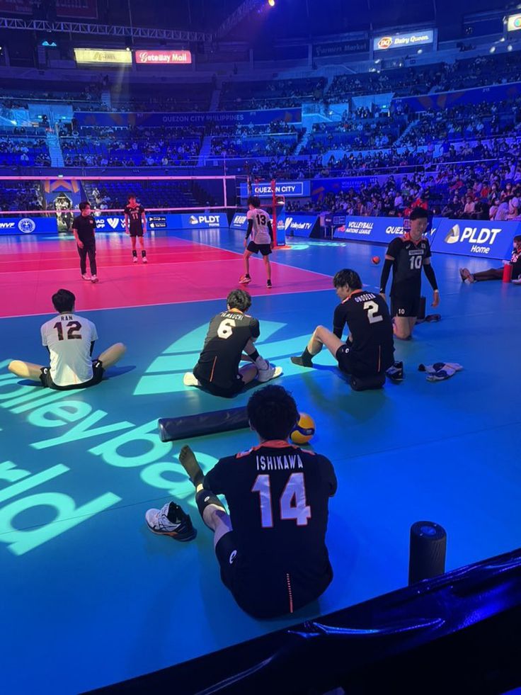 some people sitting on the floor in front of an audience at a volleyball game with numbers painted on it