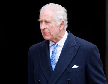 an older man in a blue suit and tie walking towards the camera with his hand on his hip