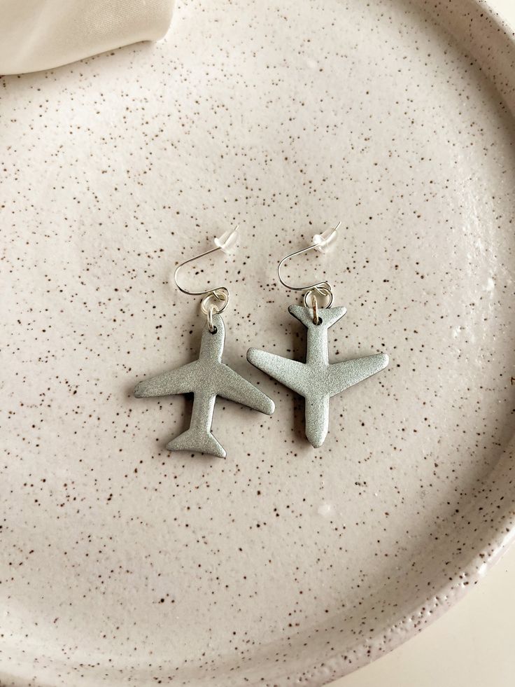 pair of silver airplane earrings on white plate