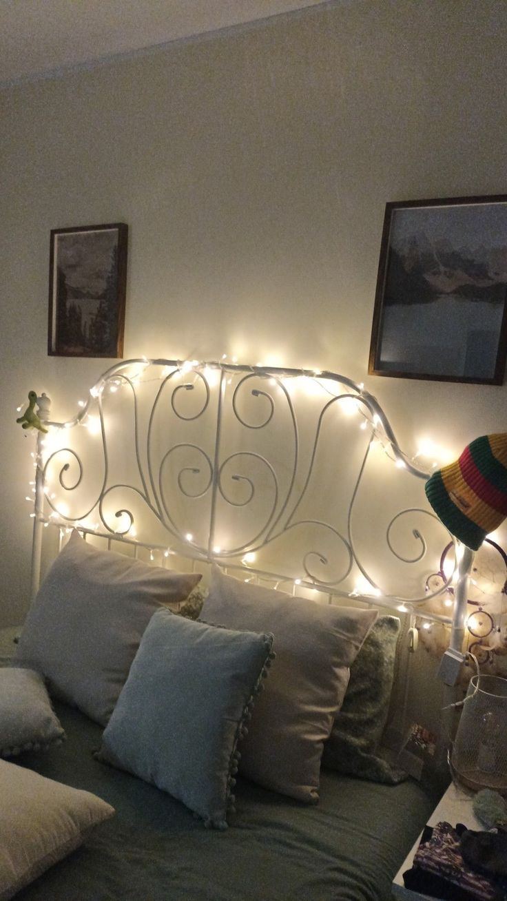 a bed that has some lights on the headboard and pillows in front of it