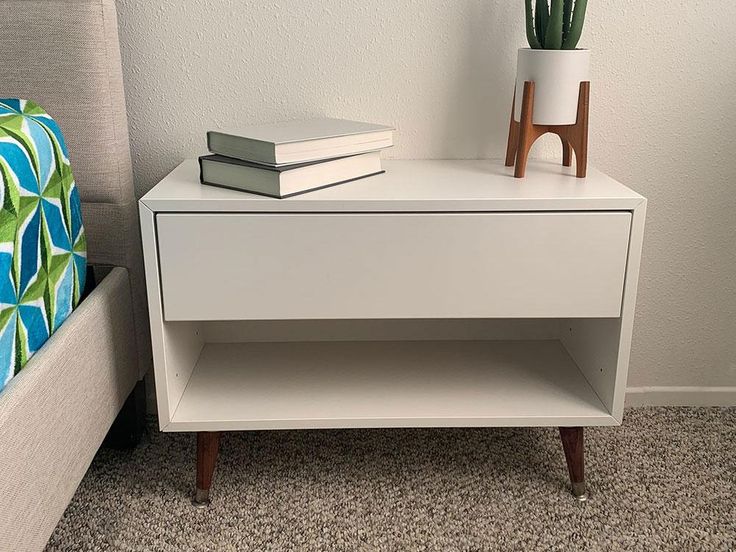 a white nightstand with two books on it next to a green pillow and a bed