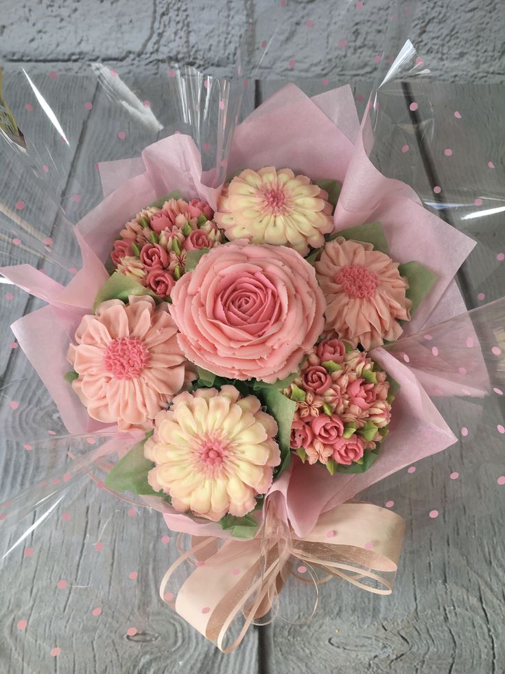 a bouquet of pink and yellow flowers in a clear vase on a wooden table with polka dots