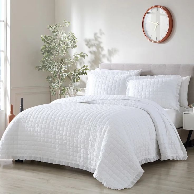 a bed with white comforter and pillows in a room next to a clock on the wall