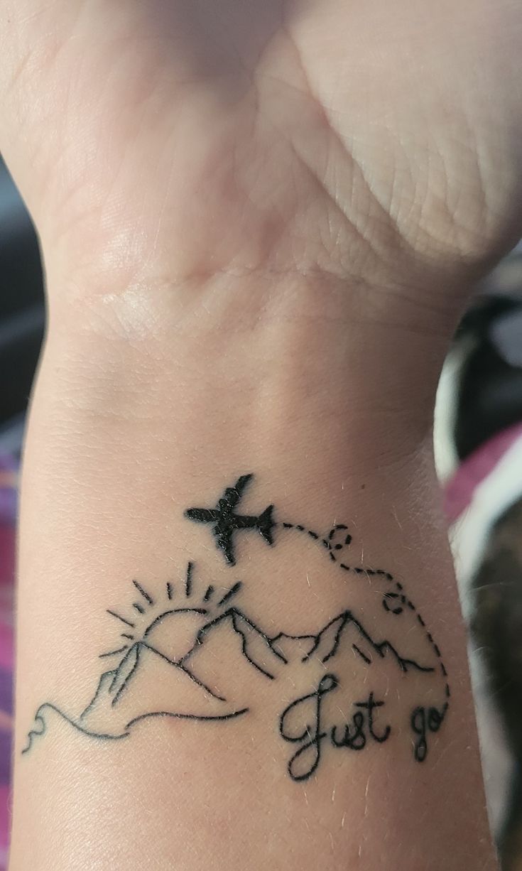 a person with a tattoo on their wrist that says just go and an airplane flying over the mountain