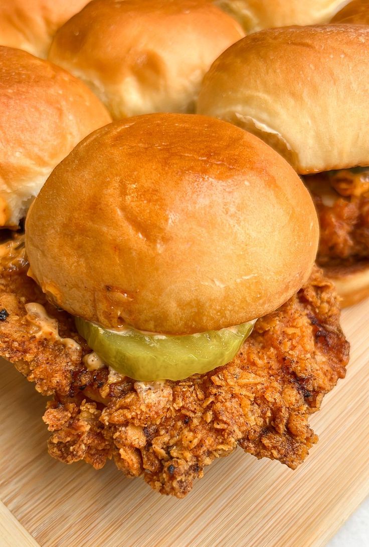 three chicken sandwiches with pickles on a cutting board next to buns that have been cut in half