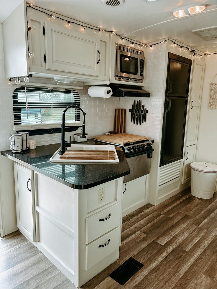 a kitchen area with white cabinets and black counter tops, lights strung from the ceiling