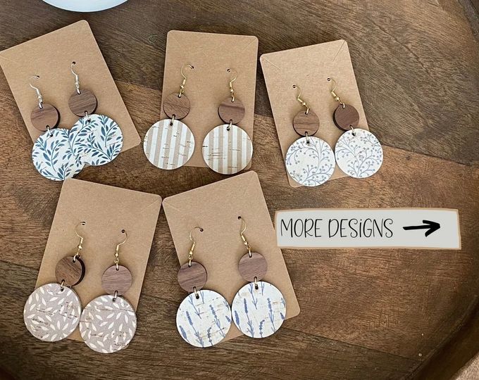 six pairs of earrings are displayed on a table with a sign that says more designs