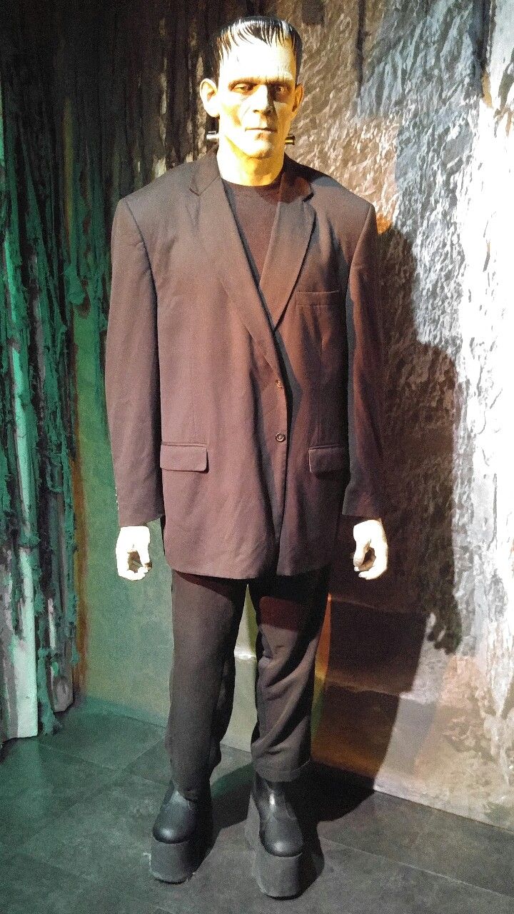 a mannequin wearing a suit and tie standing in front of a stone wall