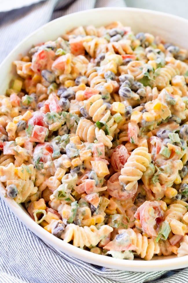 a bowl filled with pasta salad on top of a blue and white table cloth next to a fork