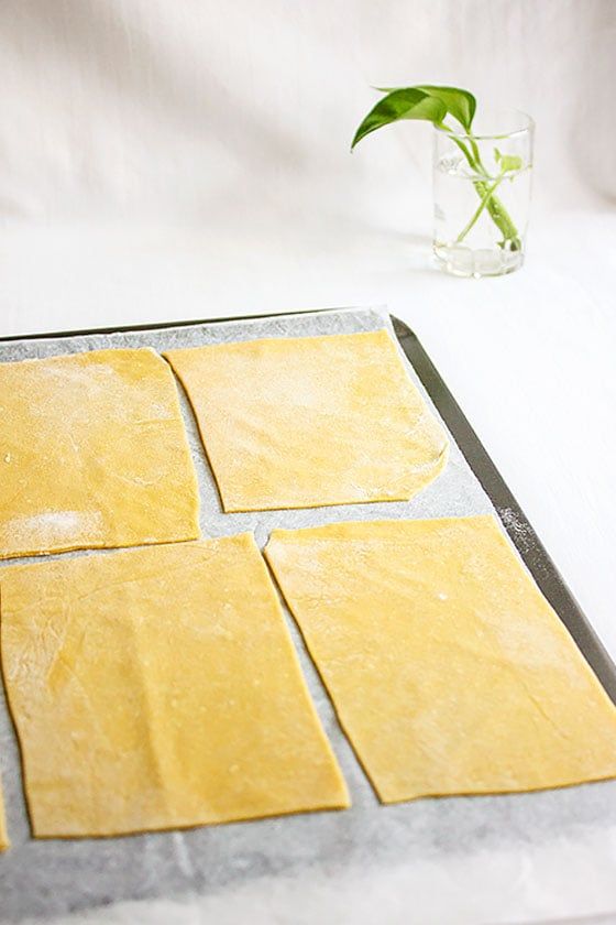 four square pieces of dough on a baking sheet next to a flower in a glass vase