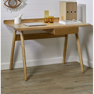 a wooden desk with a laptop and other items on it next to a white wall