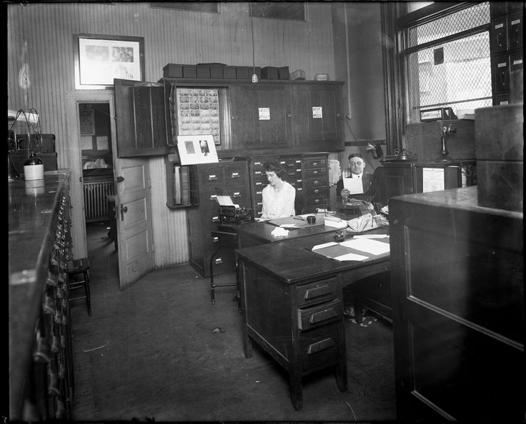 an old black and white photo of two women working at a desk with filing cabinets