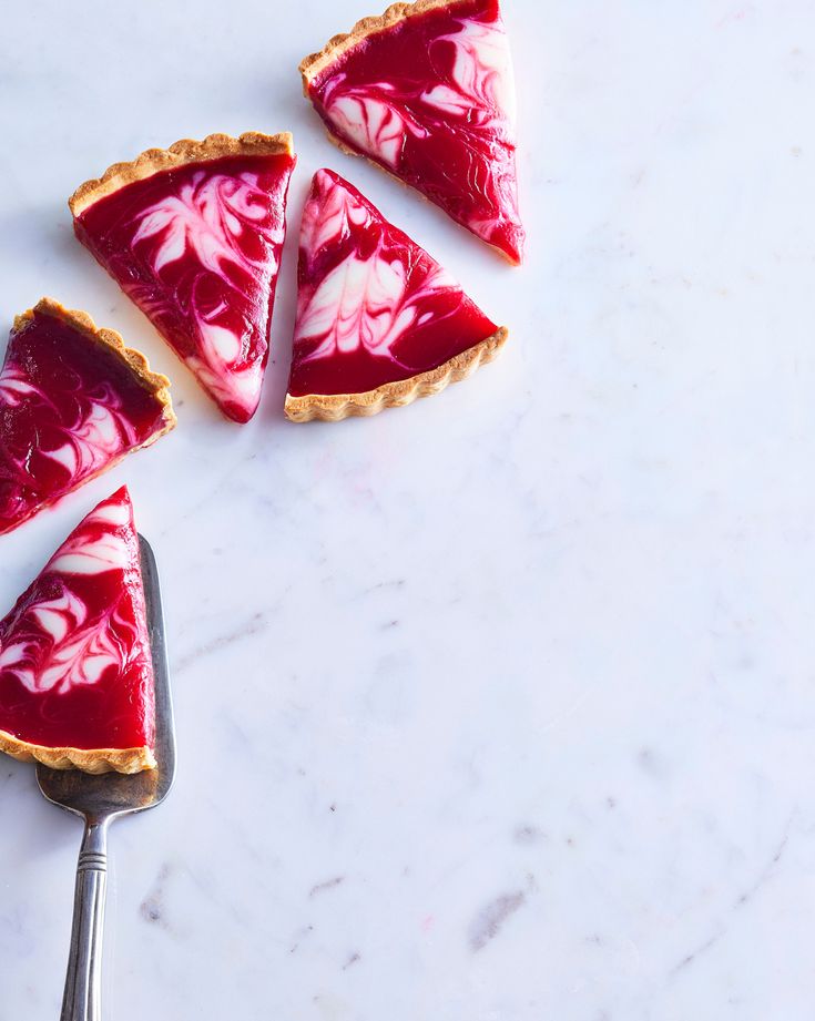 four slices of raspberry cheesecake on a marble counter top with a spoon