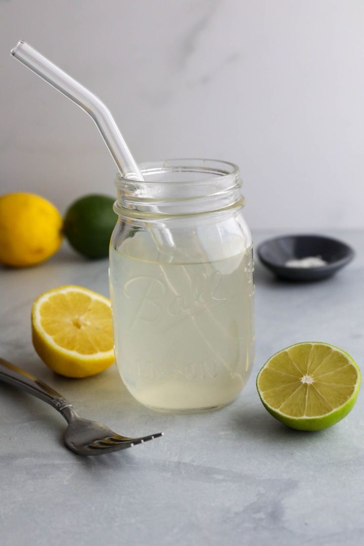 a mason jar filled with lemonade next to limes and a spoon on a table