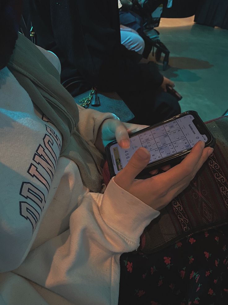 a person holding a cell phone in their hand while wearing a hoodie and sitting down