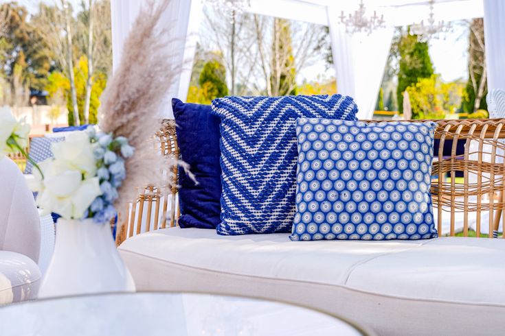 blue and white pillows sitting on top of a couch next to a vase with flowers