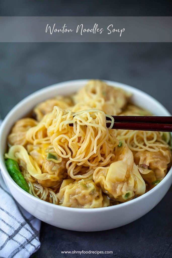 a white bowl filled with noodles and meats next to chopsticks on a table