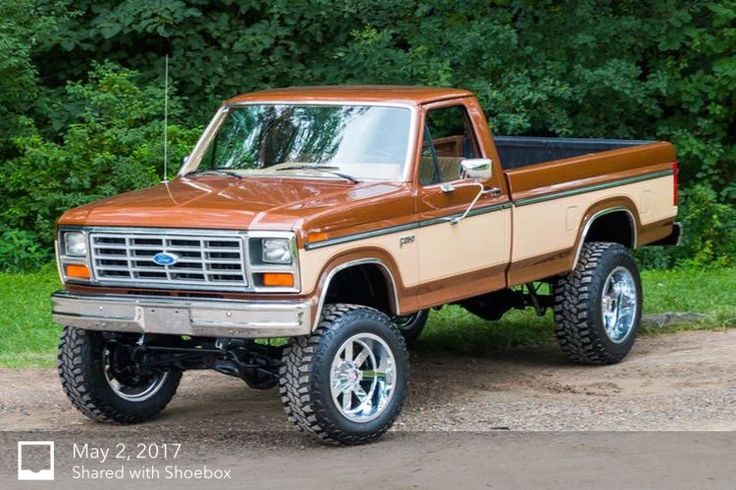 a brown truck parked on top of a dirt road next to green grass and trees