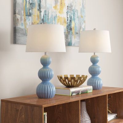 two lamps sitting on top of a wooden table next to a book shelf with books