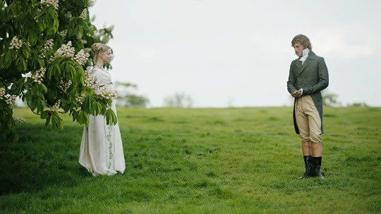 a man and woman standing next to each other on a lush green field under a tree