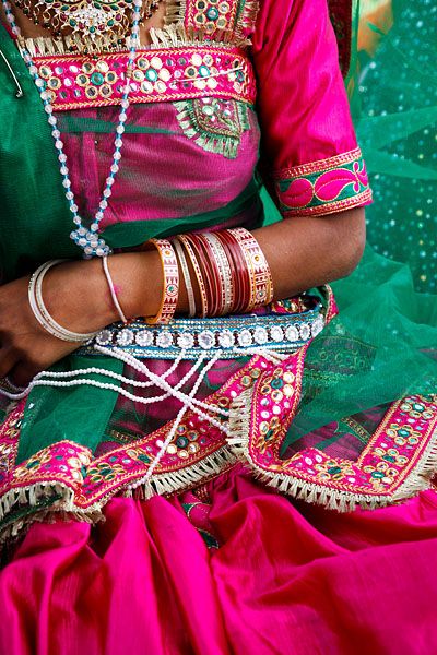 a woman in a green and pink sari sitting on the ground with her hands together