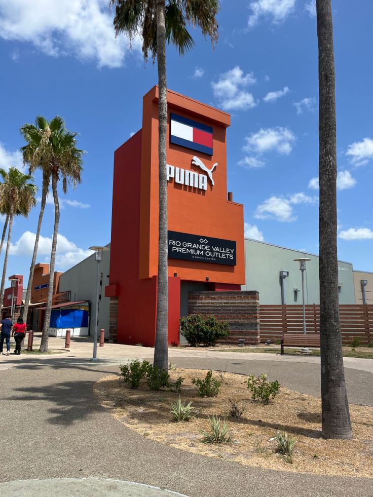 an orange building with palm trees in front of it and people walking around the area