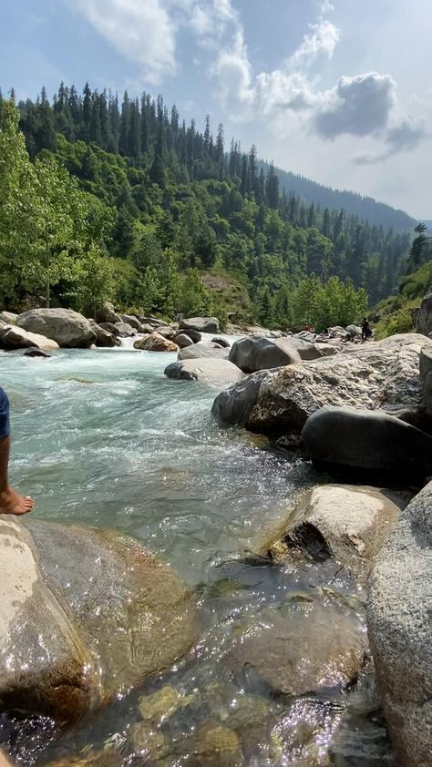 a man sitting on top of a large rock next to a river filled with water